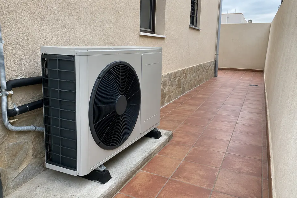Unidad exterior de aerotermia en un lateral de vivienda con pavimento de terracota