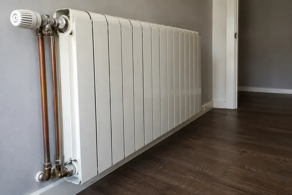 Radiador de aluminio con válvula termostática y conexiones de calefacción en una vivienda